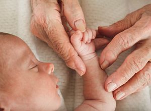great grandmother holds sleeping baby’s hand
